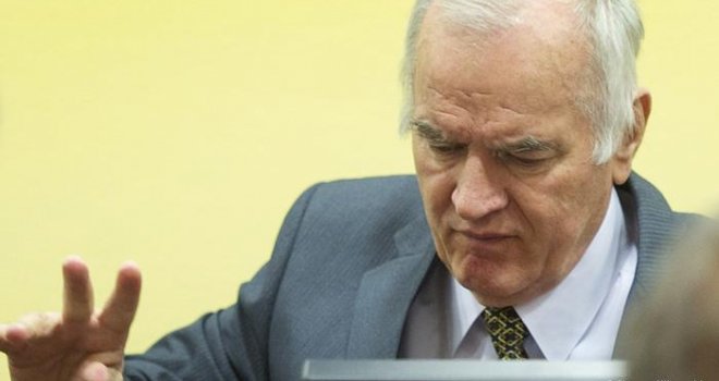 U sudnici Ratko Mladić ne nosi uniformu, odbija da skine bejzbol kapu, iz dosade lista novine i zlobno se krevelji